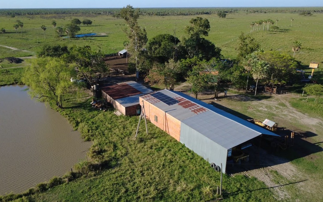 Vista aérea de un campo en Formosa con paneles solares instalados sobre el techo de un galpón junto a una laguna